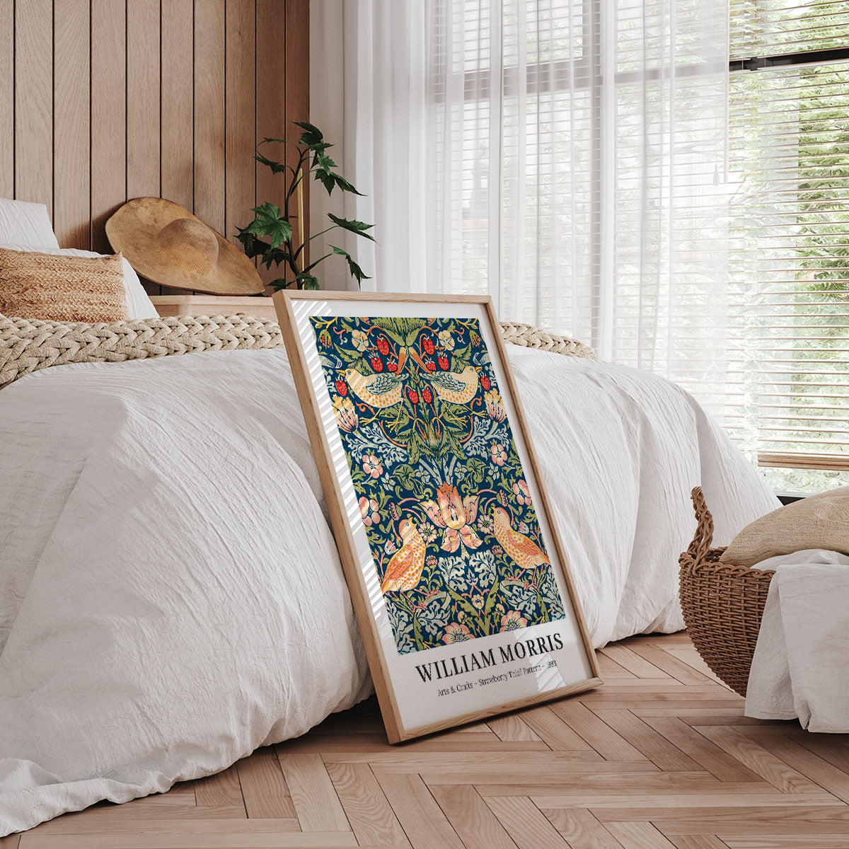 William Morris plakat med botanisk design, placeret i en ramme på et soveværelsesgulv ved siden af en seng.