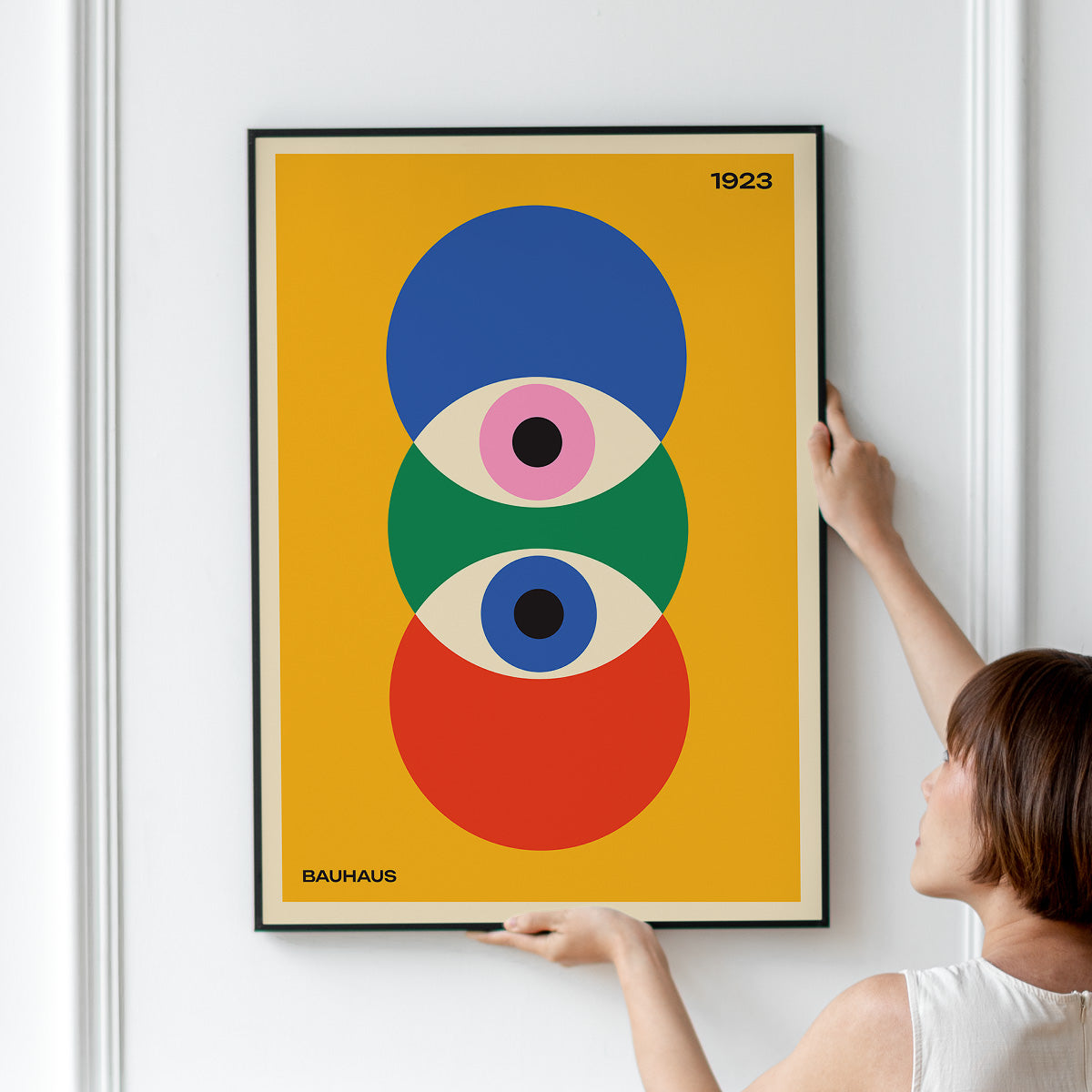 Plakat med Bauhaus-design fra 1923, viser geometriske former i blå, grøn og rød på gul baggrund, hængt op på en væg.