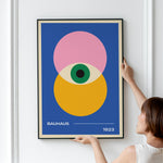 Plakat med Bauhaus-design fra 1923, viser geometriske former i pink, gul og blå med et centralt øje.