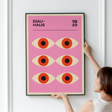 Plakat med Bauhaus-design fra 1923, viser seks stiliserede øjne på en lyserød baggrund.