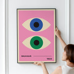 Plakat med to stiliserede øjne i blå og grøn på en lyserød baggrund, med teksten "Bauhaus 1923".