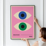 Plakat med to stiliserede øjne i blå og grøn på en lyserød baggrund, med teksten "Bauhaus 1923".
