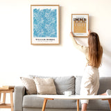 Kvinde hænger en Gustav Klimt-plakat op på en væg ved siden af en William Morris-plakat i en stue.