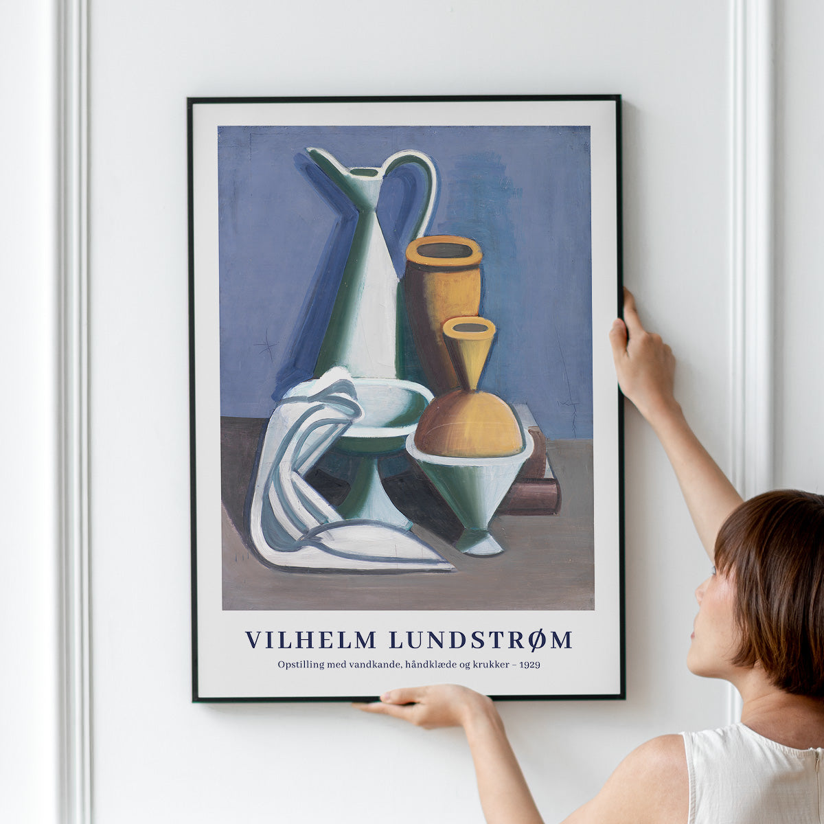 Plakat af Vilhelm Lundstrøm med titlen "Opstilling med vandkande, håndklæde og krukker - 1929" hænges op på en væg.