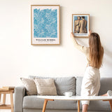 Kvinde hænger en plakat op på en væg ved siden af en William Morris plakat.