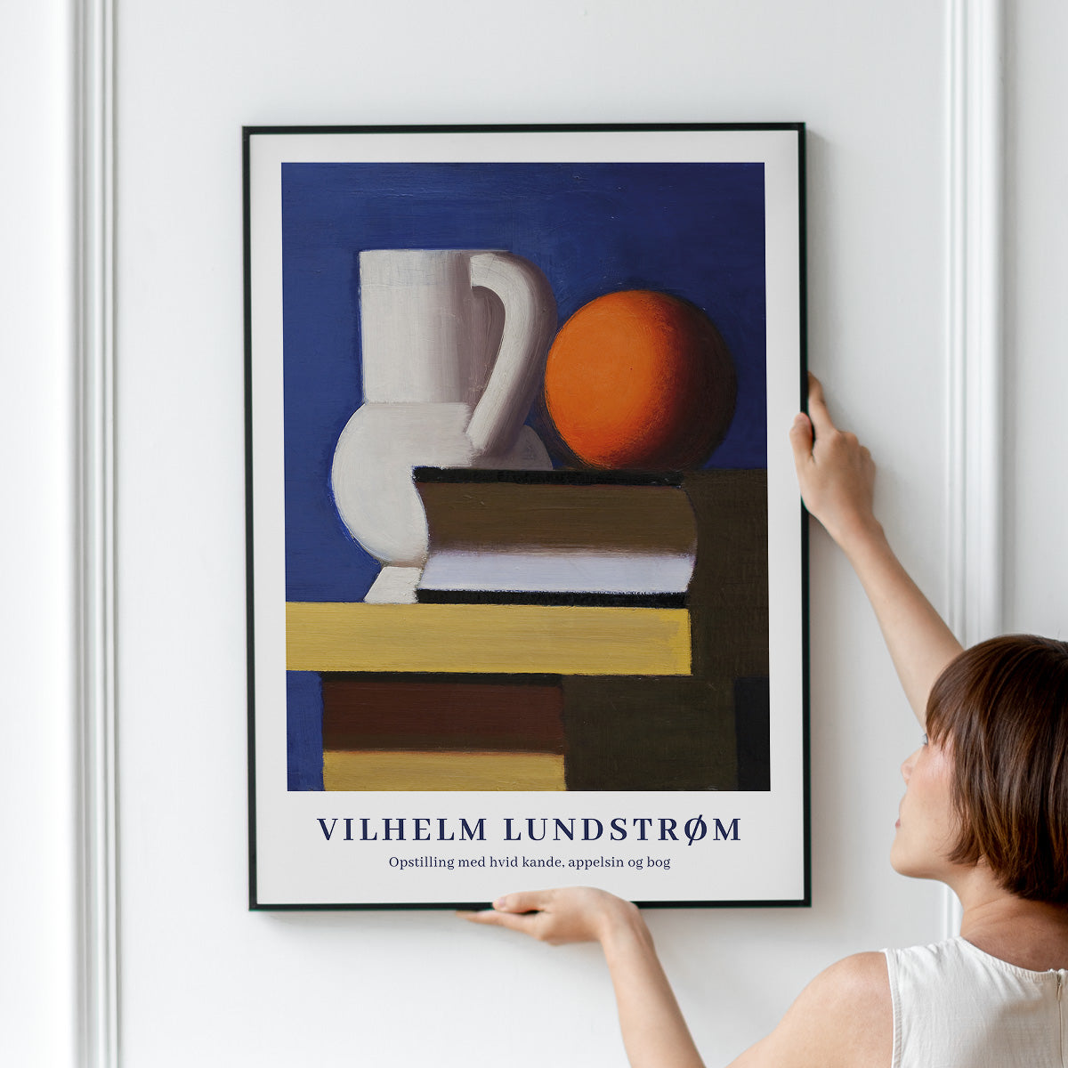 Plakat af Vilhelm Lundstrøm med titlen "Opstilling med hvid kande, appelsin og bog" hængt op på en væg.