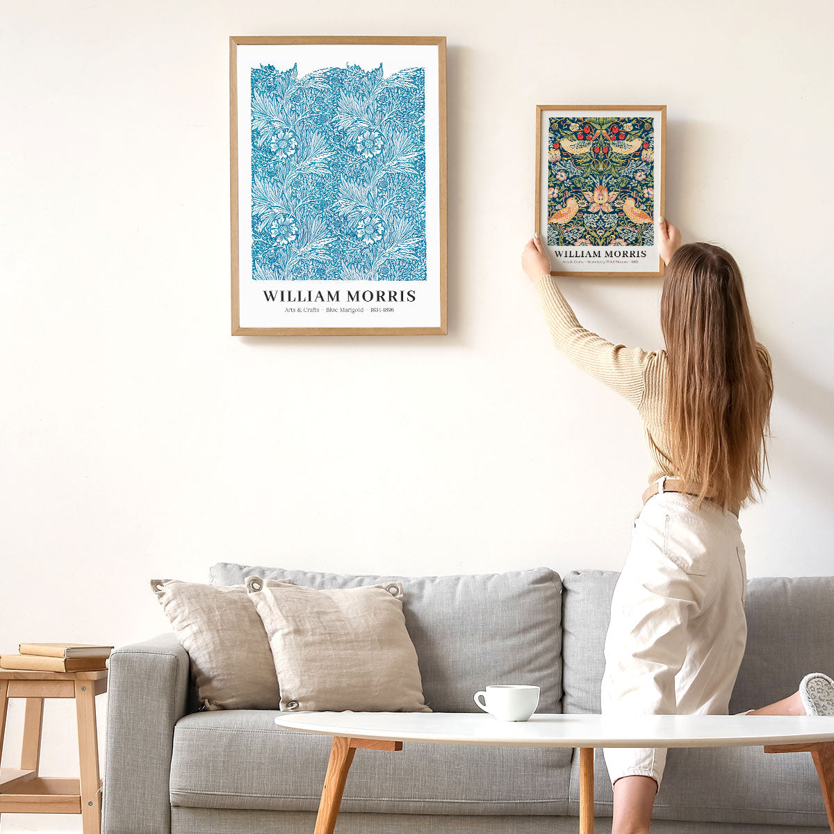 Kvinde hænger William Morris-plakat op på væggen over en sofa.