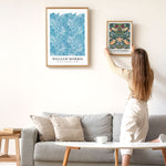 Kvinde hænger William Morris-plakat op på væggen over en sofa.