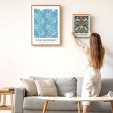 Kvinde hænger William Morris-plakat op på væggen over en sofa.