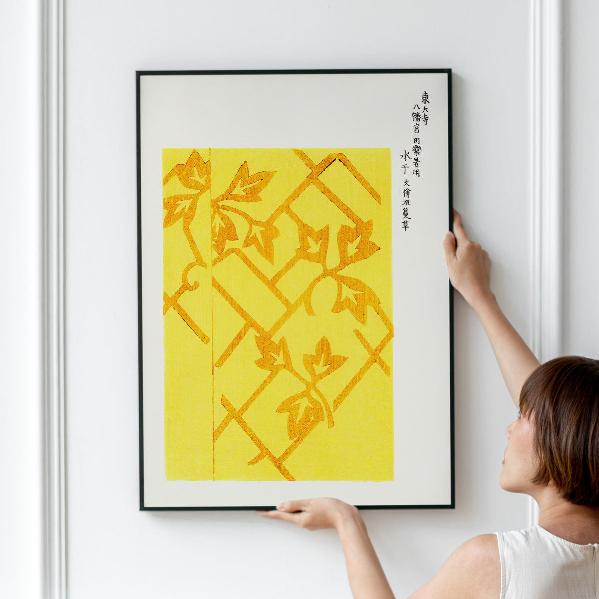 Plakat med gult og orange bladmønster hænges op på en væg.