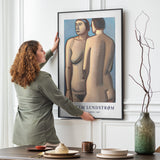 Kvinde hænger en plakat op på en væg i en stue. Plakaten viser et kunstværk af Vilhelm Lundstrøm med to figurer.