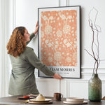 Kvinde hænger en William Morris plakat med titlen "Wild Tulip" op på en væg i en stilfuld stue.
