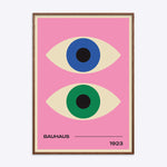 Plakat med to stiliserede øjne i blå og grøn på en lyserød baggrund, med teksten "Bauhaus 1923" nederst, indrammet i mørk naturtræsramme.