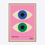 Bauhaus plakat med to stiliserede øjne i blå og grøn på en lyserød baggrund, indrammet i naturtræ.