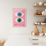 Plakat i træramme i køkken med Bauhaus-design, lyserød baggrund og to stiliserede øjne.