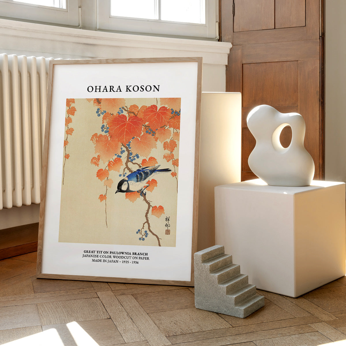 Plakat af Ohara Koson med motiv af en mejse på en gren med orange blade, placeret på et gulv ved siden af moderne skulpturer.
