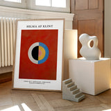 Hilma af Klint plakat med abstrakt design, placeret på et trægulv ved siden af en moderne skulptur.