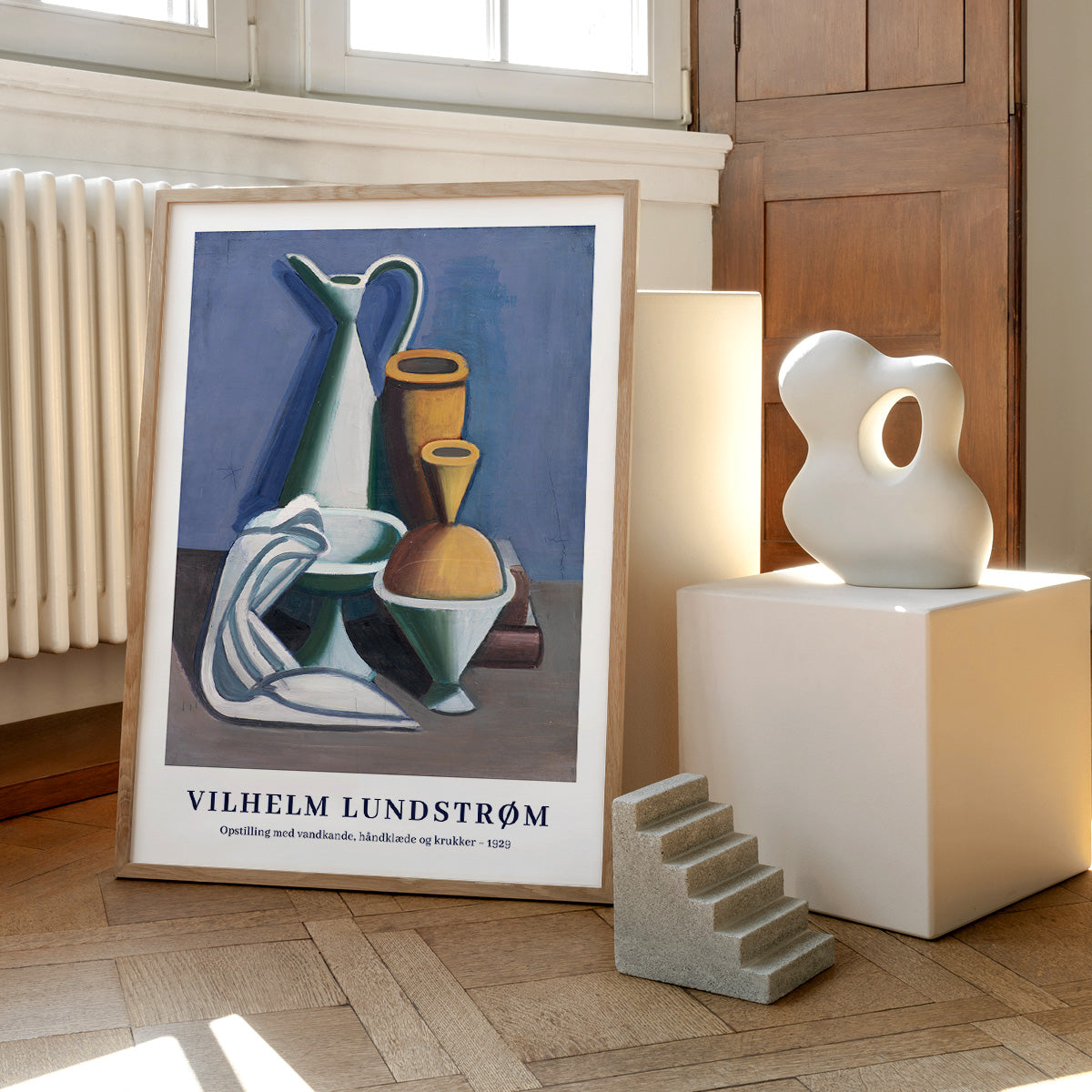 Plakat af Vilhelm Lundstrøm med titlen "Opstilling med vandskål, håndklæde og krukker - 1930" placeret på et trægulv ved siden af en skulptur og en lille trappe.