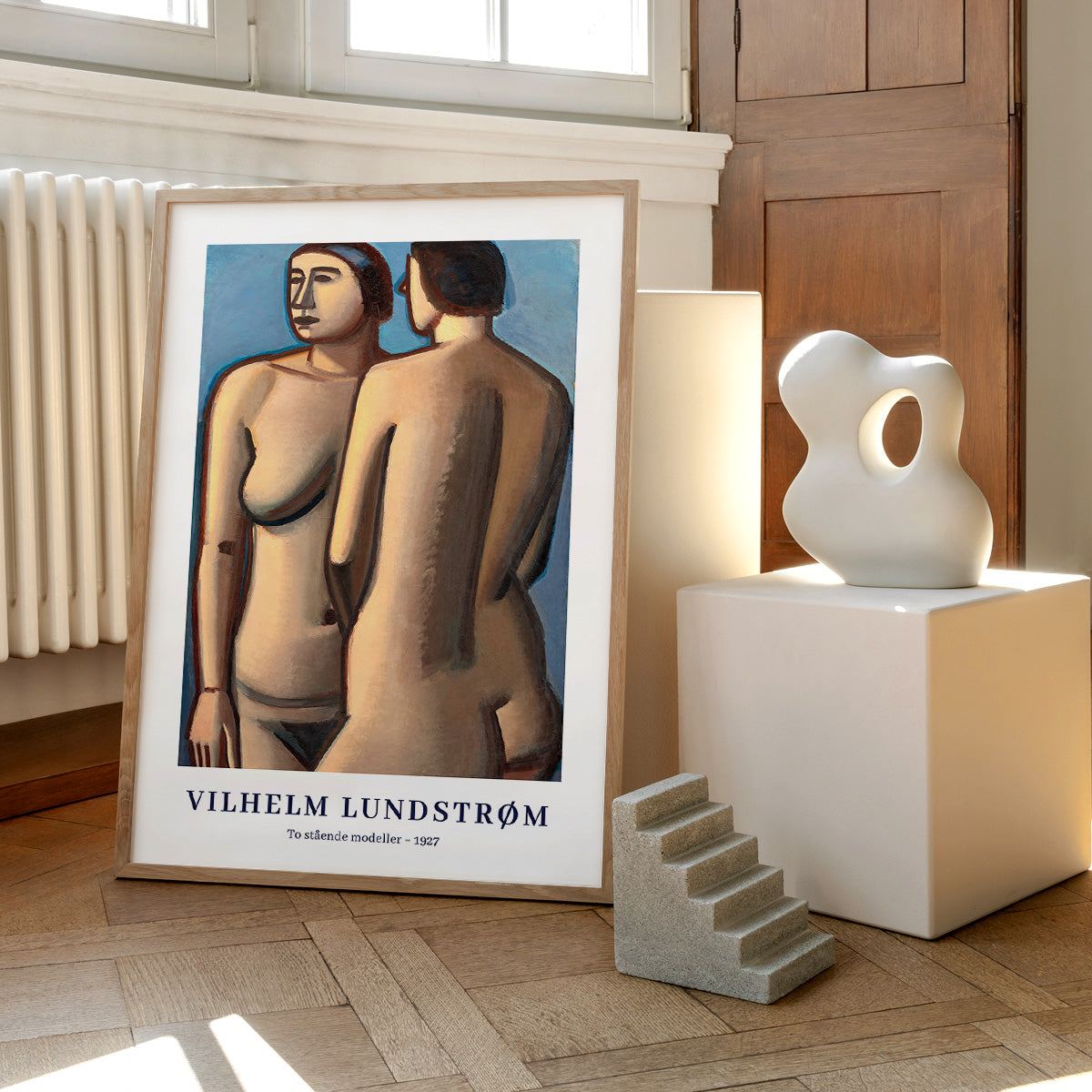 Plakat af Vilhelm Lundstrøm med titlen "To stående modeller - 1927" placeret på et trægulv ved siden af en moderne skulptur og en lille trappeformet dekoration.