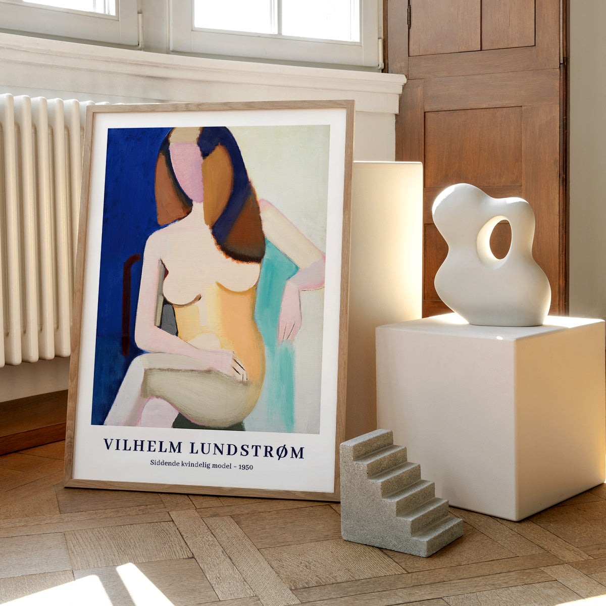 Plakat af Vilhelm Lundstrøm med titlen "Sidende kvindelig model - 1950" placeret på et trægulv ved siden af en skulptur og en lampe.