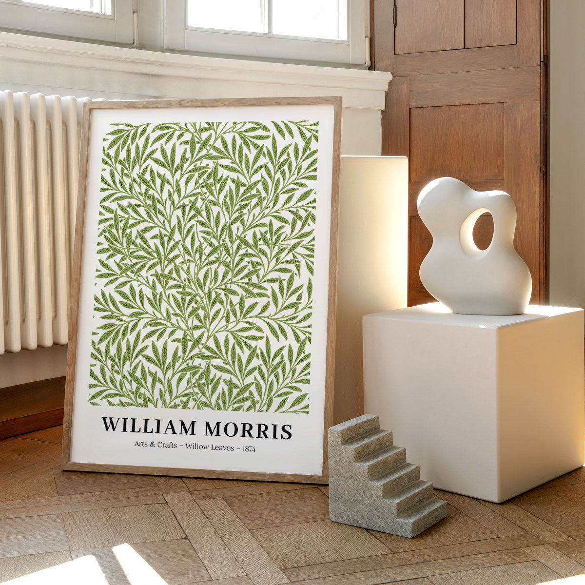 William Morris plakat med grønne pileblade, placeret på et trægulv ved siden af moderne skulpturer.