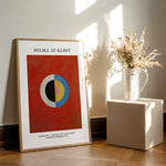 Hilma af Klint plakat med abstrakt design, placeret på et trægulv ved siden af en vase med tørrede blomster.