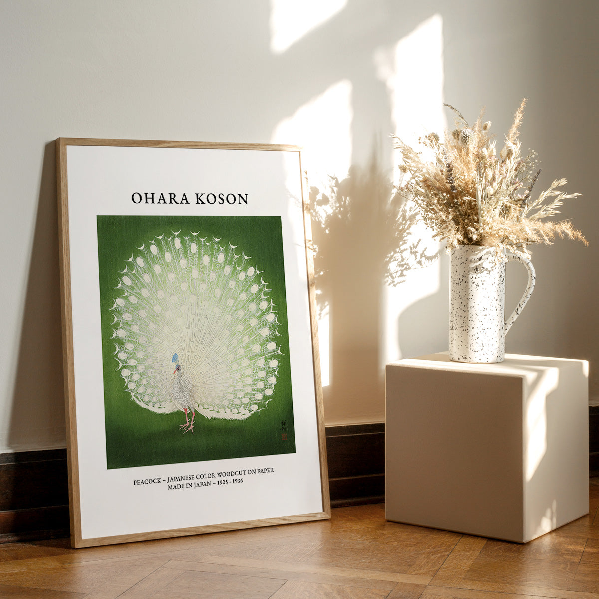 Ohara Koson plakat med påfugl, stående på gulv ved siden af en vase med tørrede blomster.