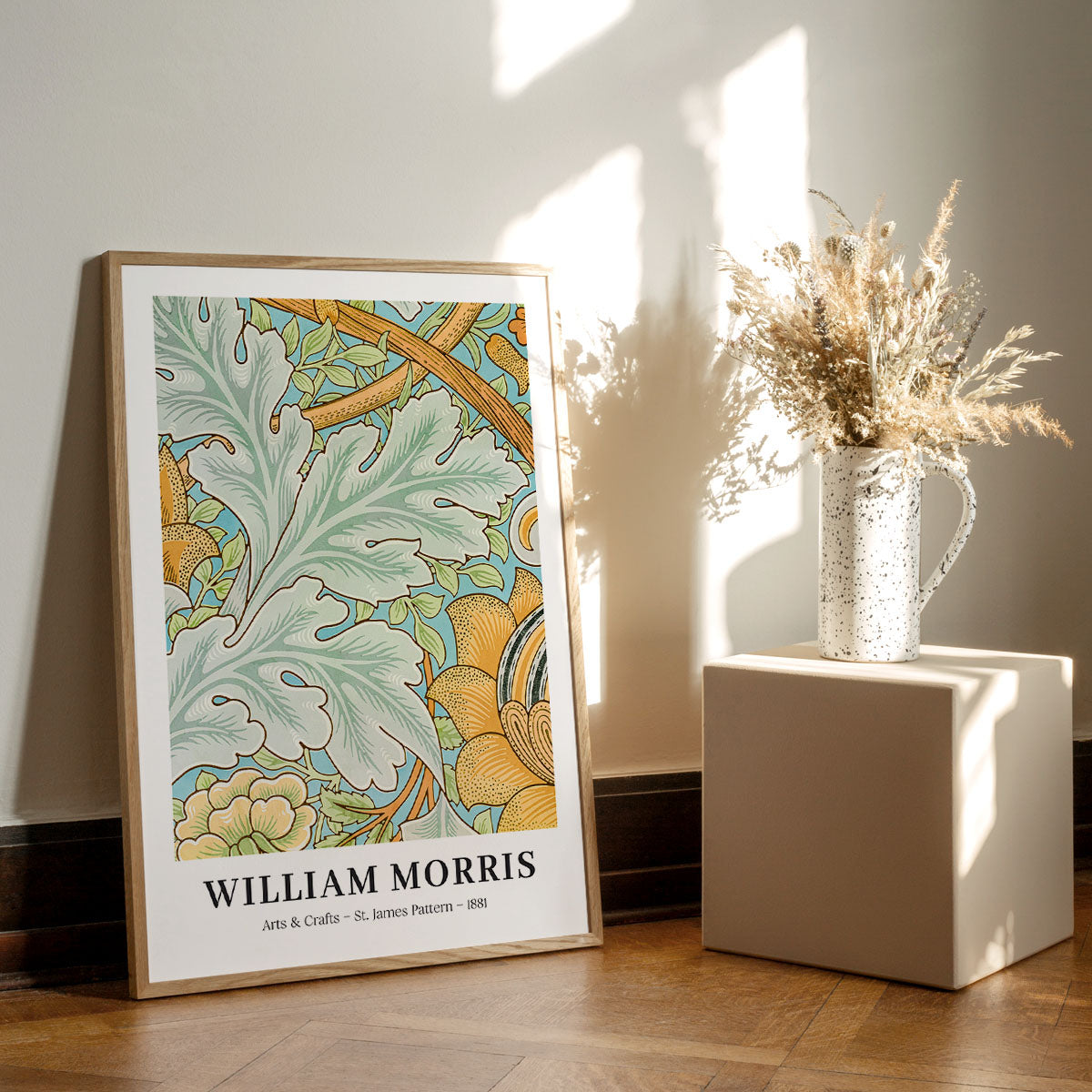 William Morris plakat med botanisk mønster, placeret på gulvet ved siden af en vase med tørrede blomster.