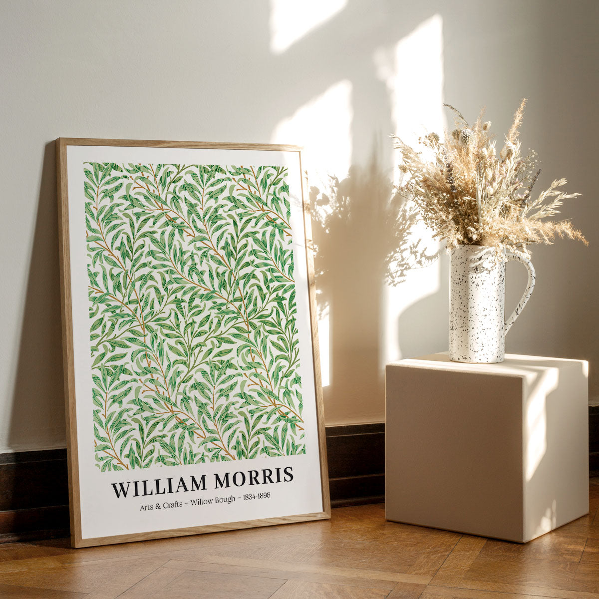 William Morris plakat med titlen "Willow Bough" fra 1887, placeret på et trægulv ved siden af en vase med tørrede blomster.