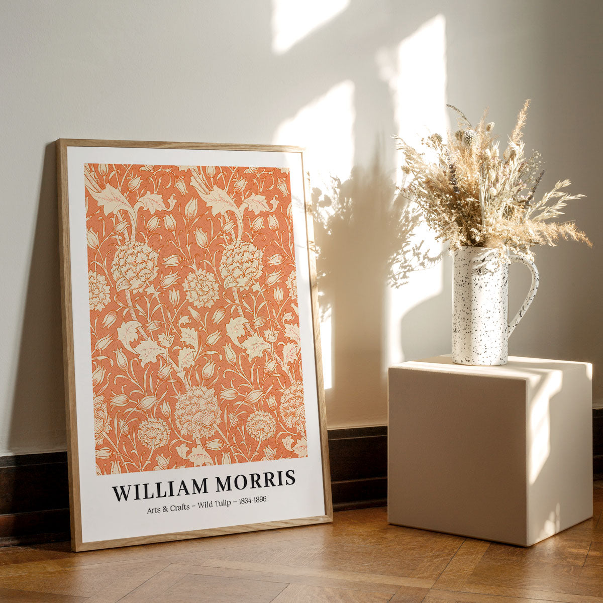 William Morris plakat med titlen "Wild Tulip" fra 1884, placeret på et trægulv ved siden af en vase med tørrede blomster.
