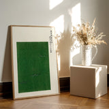 Plakat af Yatsuo Crane med et minimalistisk grønt design, placeret på et trægulv ved siden af en vase med tørrede blomster.