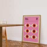 Plakat med Bauhaus-design, lyserød baggrund og seks stiliserede øjne, placeret på gulvet i en moderne stue.
