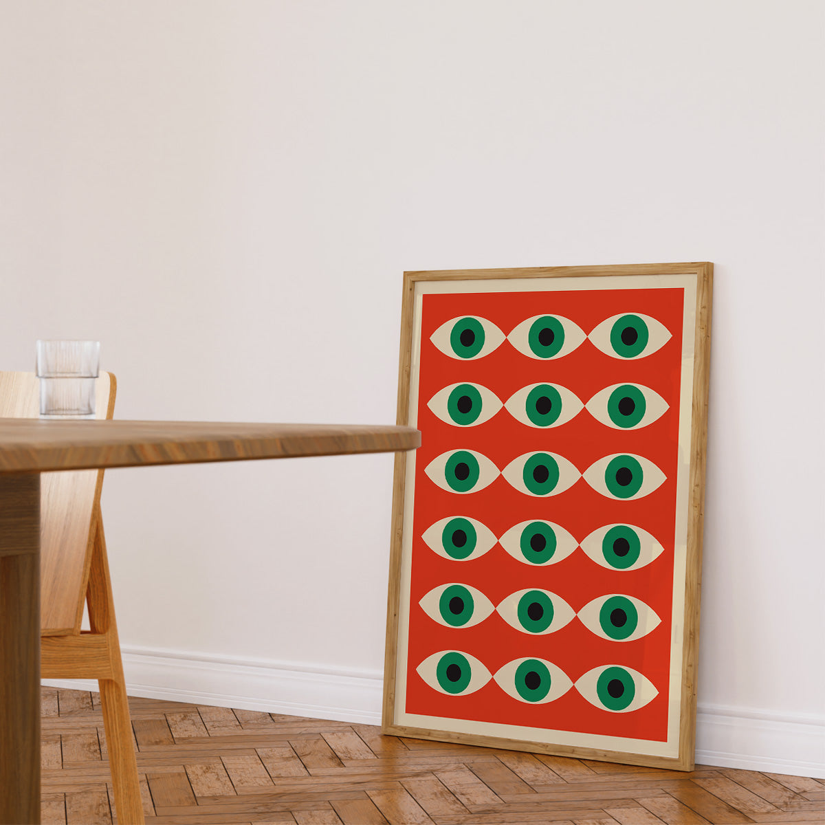 Plakat med geometrisk øjenmønster i røde og grønne farver, placeret på gulvet i en moderne stue.
