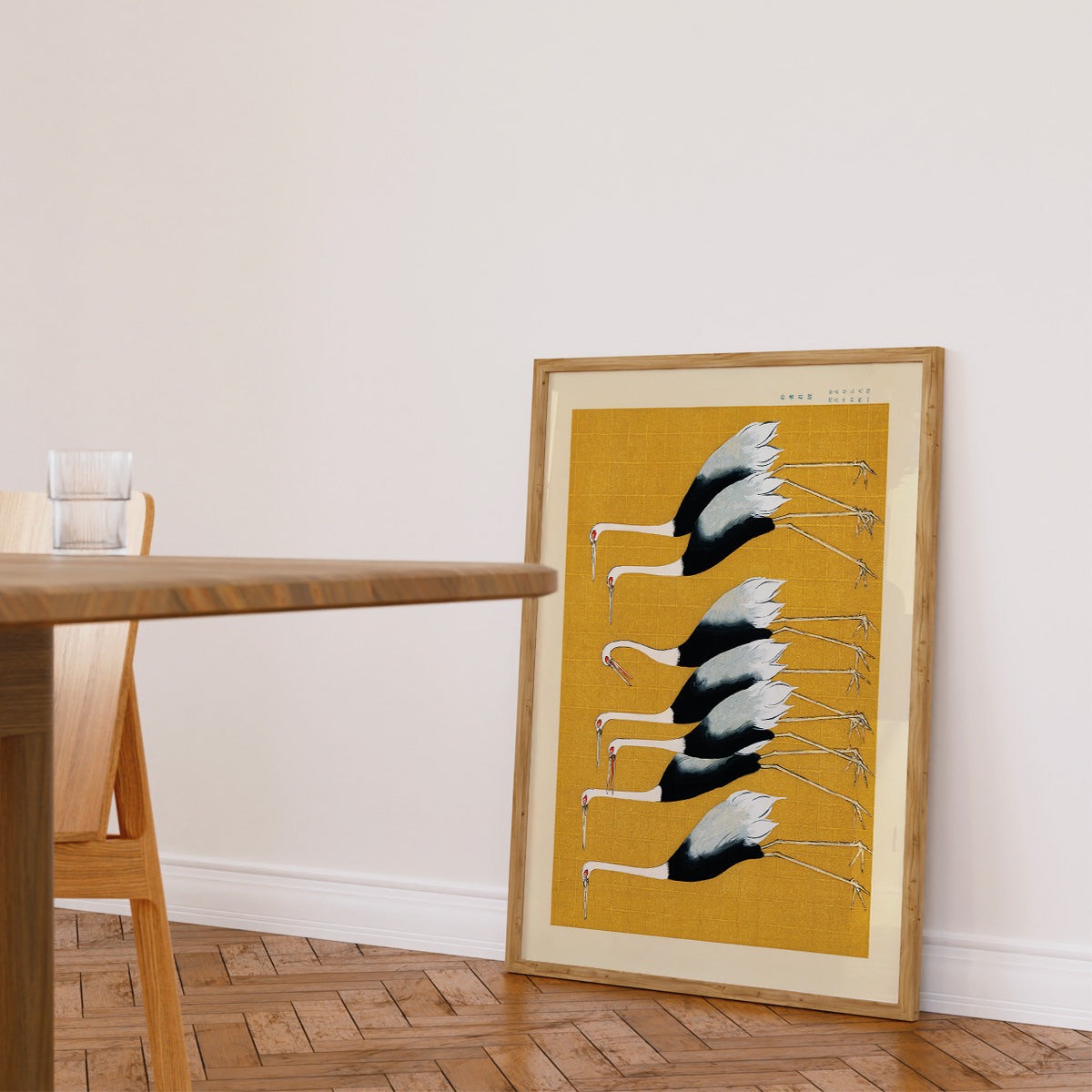 Plakat med traner i minimalistisk stil, placeret på gulvet ved siden af et træbord i en stue.