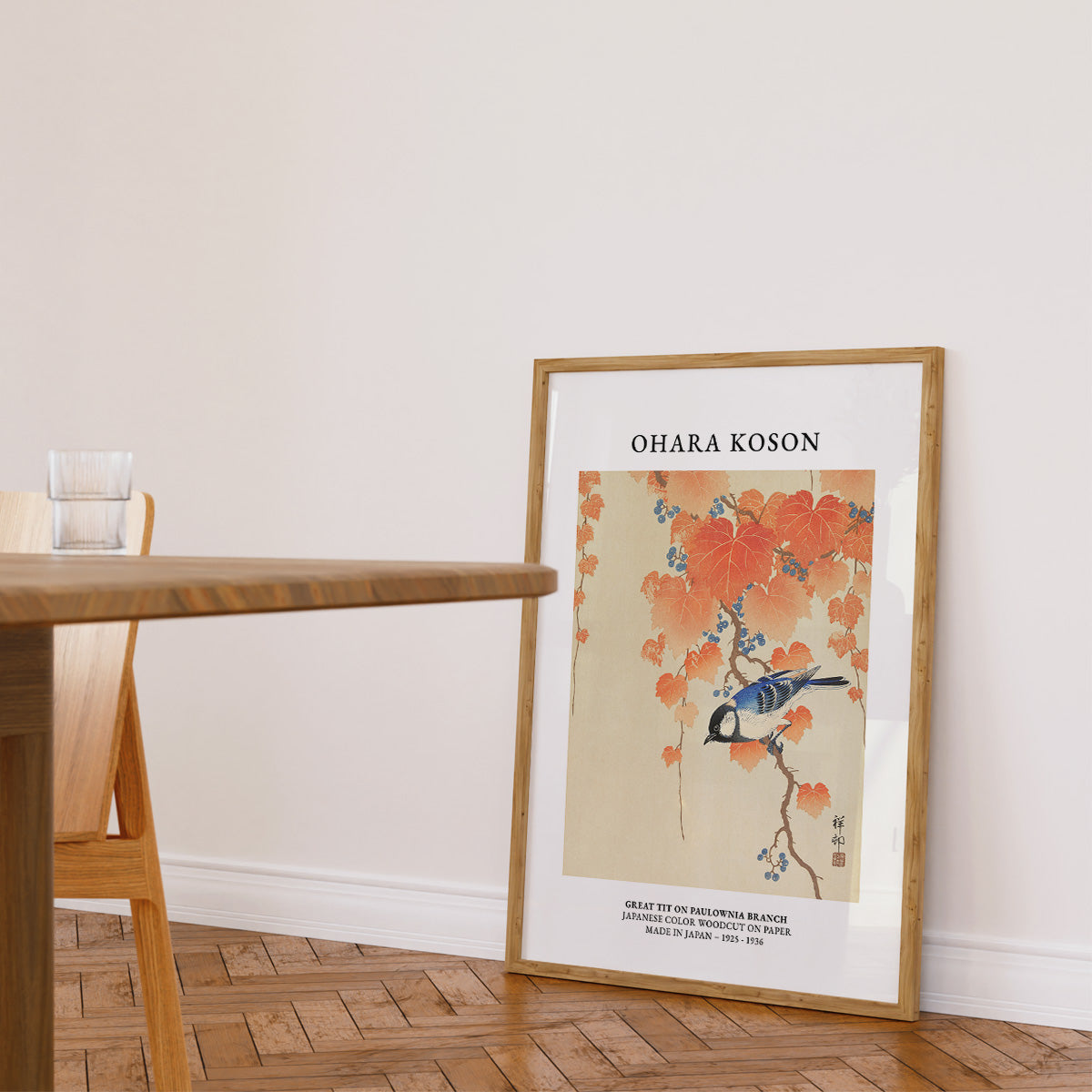Plakat af Ohara Koson med en mejse på en gren, placeret på gulvet i en stue ved siden af et bord.