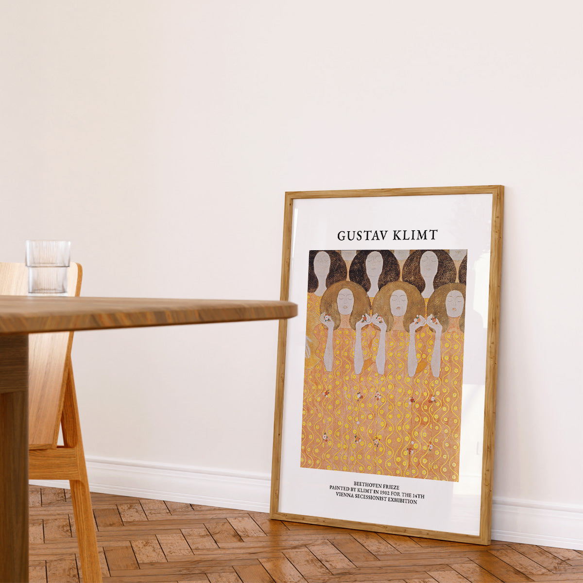 Gustav Klimt plakat i ramme, placeret på gulvet i en stue ved siden af et træbord og en stol.