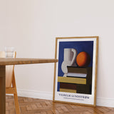 Plakat af Vilhelm Lundstrøm med stillebenmotiv, der viser en kande, en bog og en appelsin, placeret på gulvet i en moderne stue.