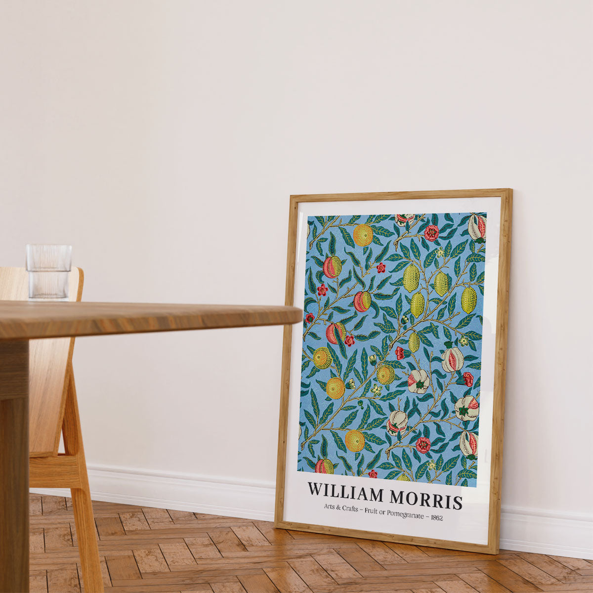 Plakat af William Morris med titlen "Fruit of Pomegranate" fra 1862, placeret på gulvet i en stue ved siden af et træbord.