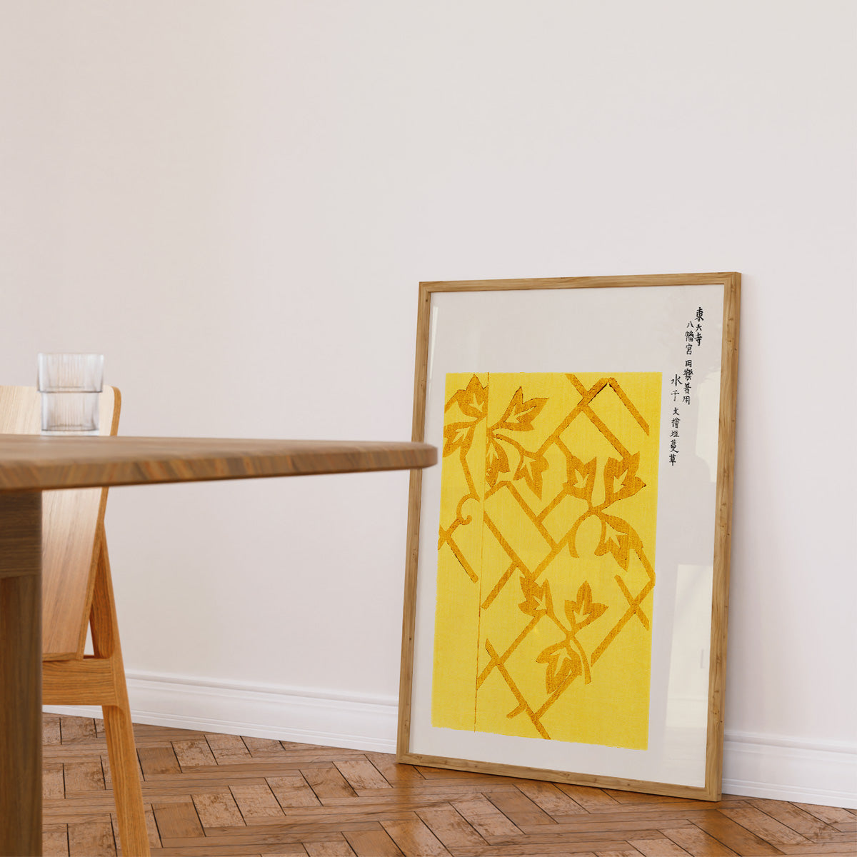Plakat med gult og orange abstrakt design i træramme, placeret på gulvet ved siden af et træbord i en lys stue.