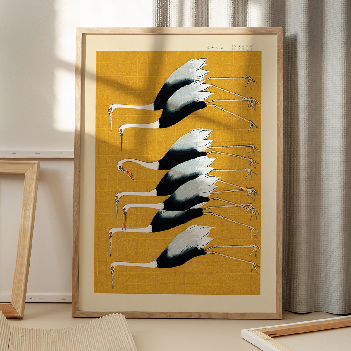 Plakat med illustration af traner på gul baggrund, placeret på gulv med skygge fra vindue.