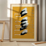 Plakat med illustration af traner på gul baggrund, placeret på gulv med skygge fra vindue.