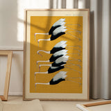 Plakat med illustration af traner på gul baggrund, placeret på gulv med skygge fra vindue.