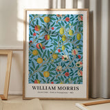 William Morris plakat med frugt- og granatæblemotiv, Arts & Crafts stil, 1862, stående på gulv med skygge fra vindue.