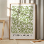 Plakat med grønne blade designet af William Morris, titlen "Willow Leaves", år 1874, placeret på et gulv med skygger fra et vindue.