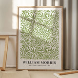 Plakat med grønne blade designet af William Morris, titlen "Willow Leaves", år 1874, placeret på et gulv med skygger fra et vindue.