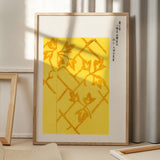 Plakat med gult mønster og japanske tegn, indrammet og placeret på gulv med skygge fra vindue.