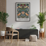 Plakat af William Morris med titlen "Strawberry Thief" hænger på en væg i en stilfuld stueindretning med planter og moderne møbler.
