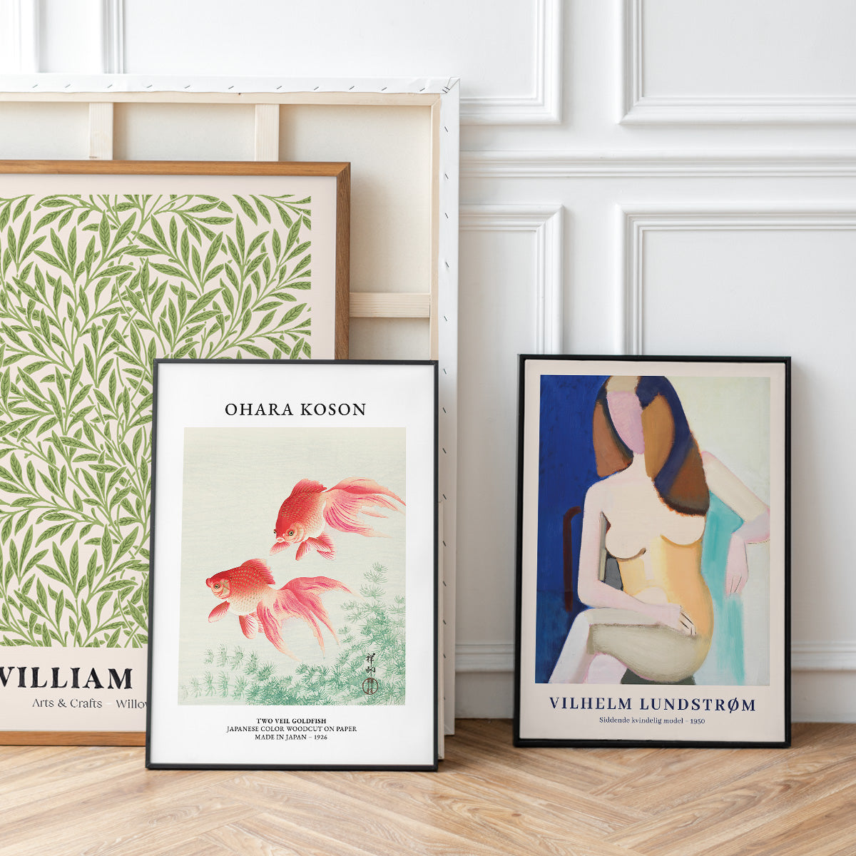 Plakater i rammer, herunder "Two Red Goldfish" af Ohara Koson og en kunstplakat af Vilhelm Lundstrøm, opstillet mod en hvid væg.