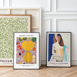 Tre kunstplakater lænet op ad en hvid væg. Den første plakat har et grønt bladmønster, den anden er af Hilma af Klint med abstrakte former, og den tredje er af Vilhelm Lundstrøm med en stiliseret figur.