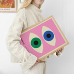 Kvinde holder en Bauhaus-plakat med et pink baggrund og to øjenlignende figurer i grøn og blå.